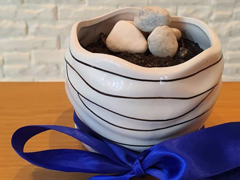 A flowerpot with soil and stones in it on a table wrapped with a blue ribbon.