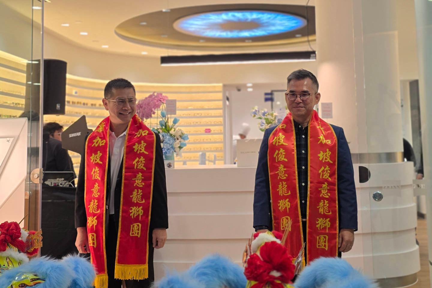 Two persons wearing red shawls are facing a light blue dragon performer at the opening ceremony of the Zeiss Vision Center in Singapore