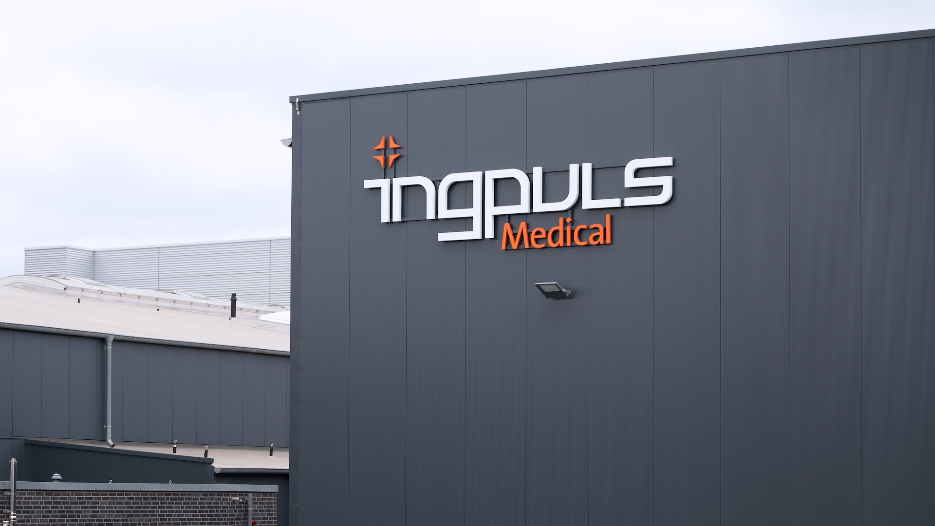 Exterior view of a modern industrial building with the logo "ingpuls Medical" displayed on the dark grey facade.