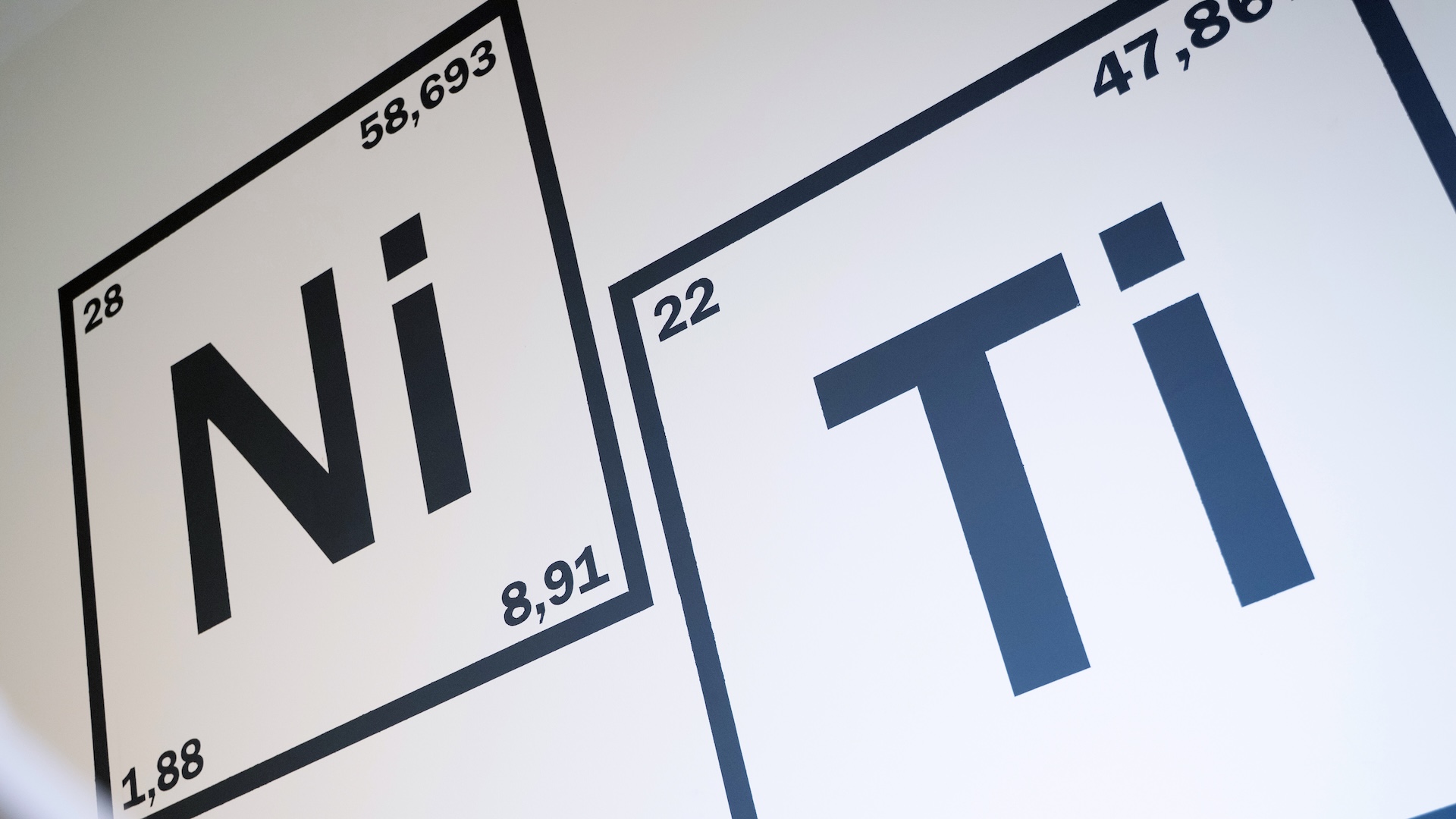 Wall graphic showing the chemical elements Nickel (Ni) and Titanium (Ti) represented as periodic table tiles.
