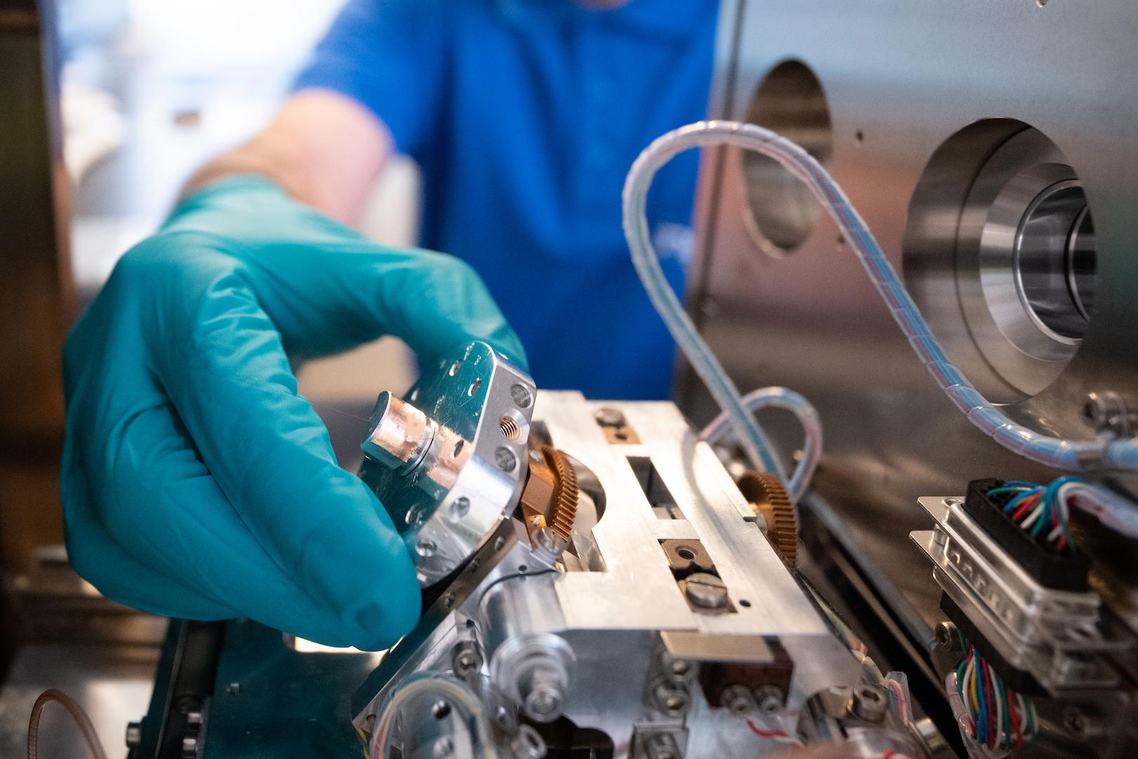 A gloved hand adjusts a precision component inside a ZEISS EVO.