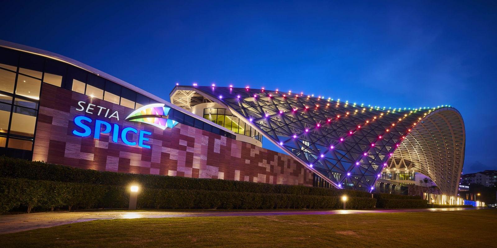 Wide staircase leading up to a modern glass building with two large blue cylindrical structures on either side, set against a dramatic sunset sky.