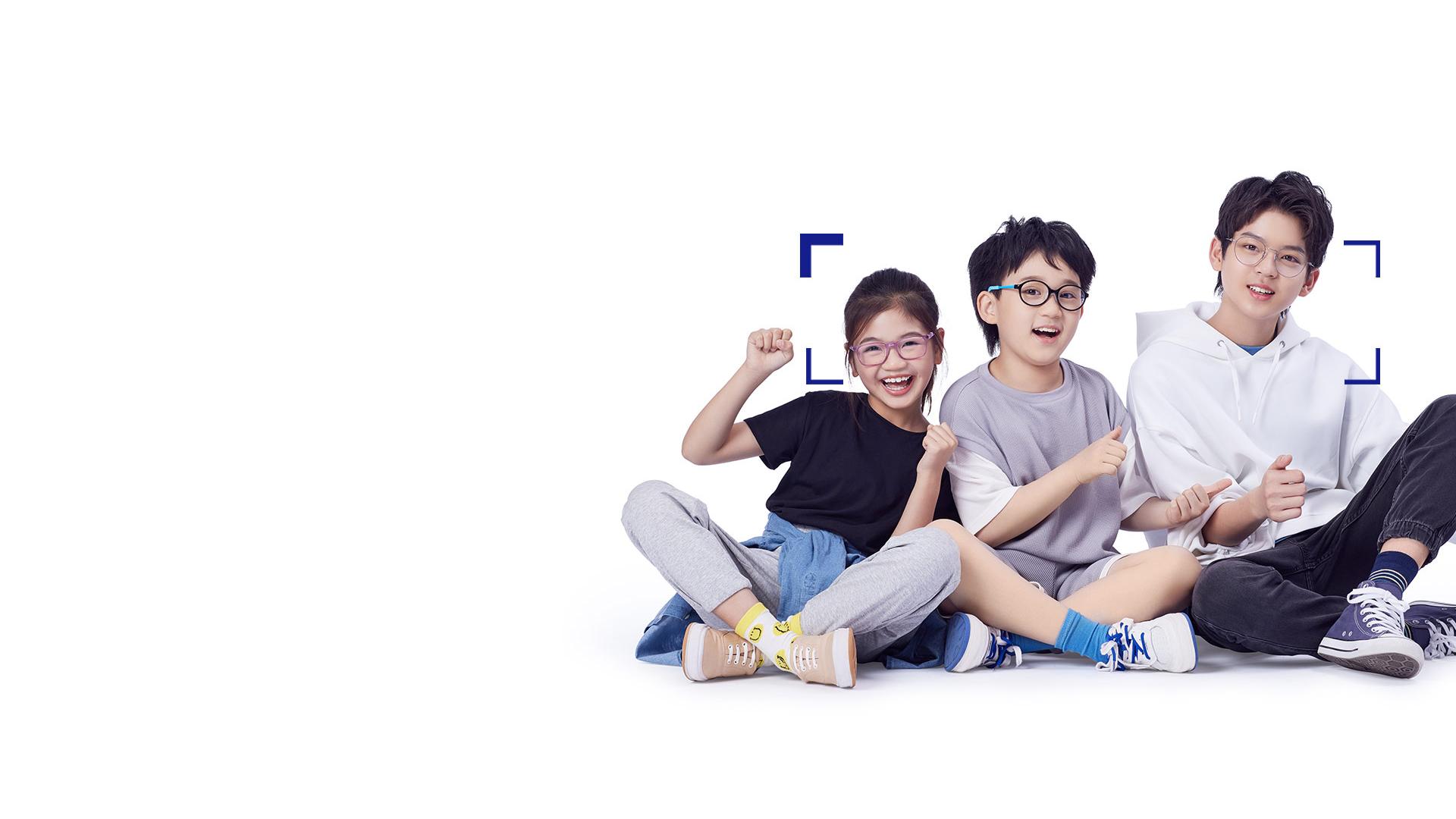 Two boys and a girl with glasses sitting next to each other laughing and giving thumbs up.