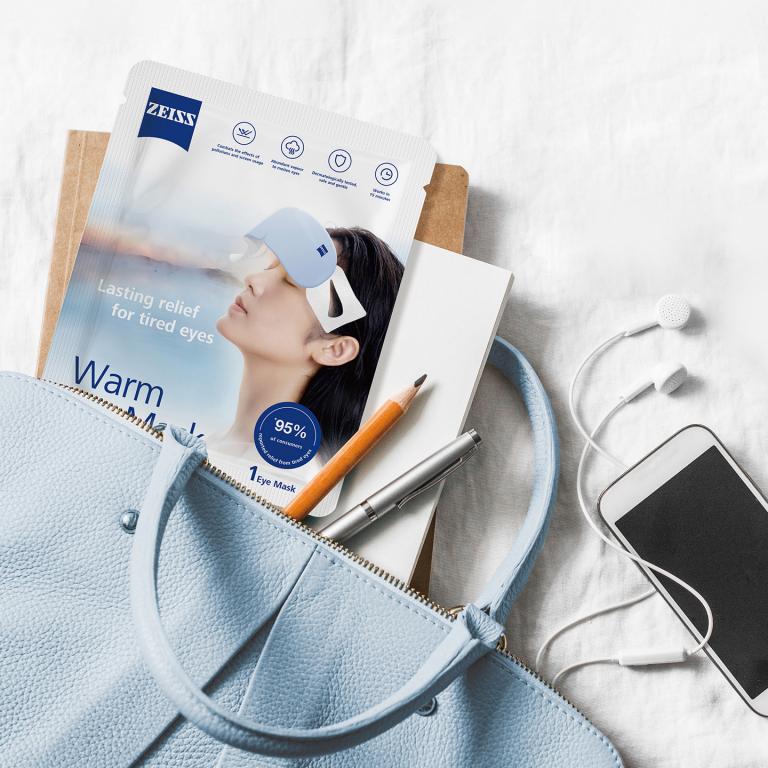 An illustration of a cosmetics bag with a packed and unpacked ZEISS Warm Eye Mask.