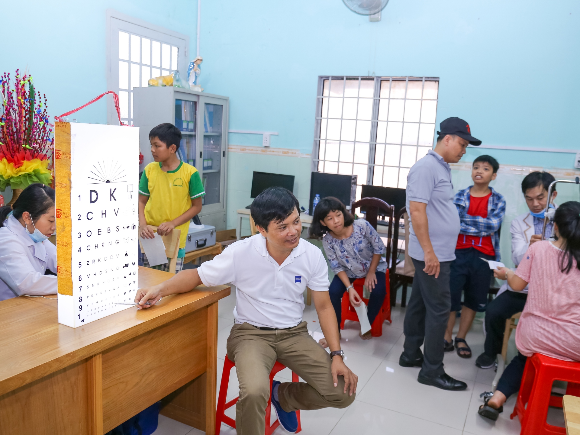 A doctor performs an eye exam on children pointing at a chart for the examination