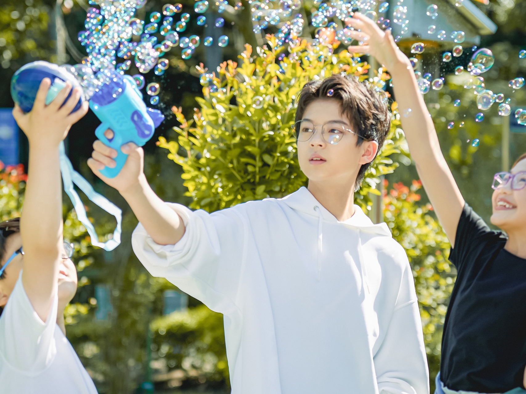A teenager and two children wearing ZEISS Myopia Management lenses playing with soap bubbles.