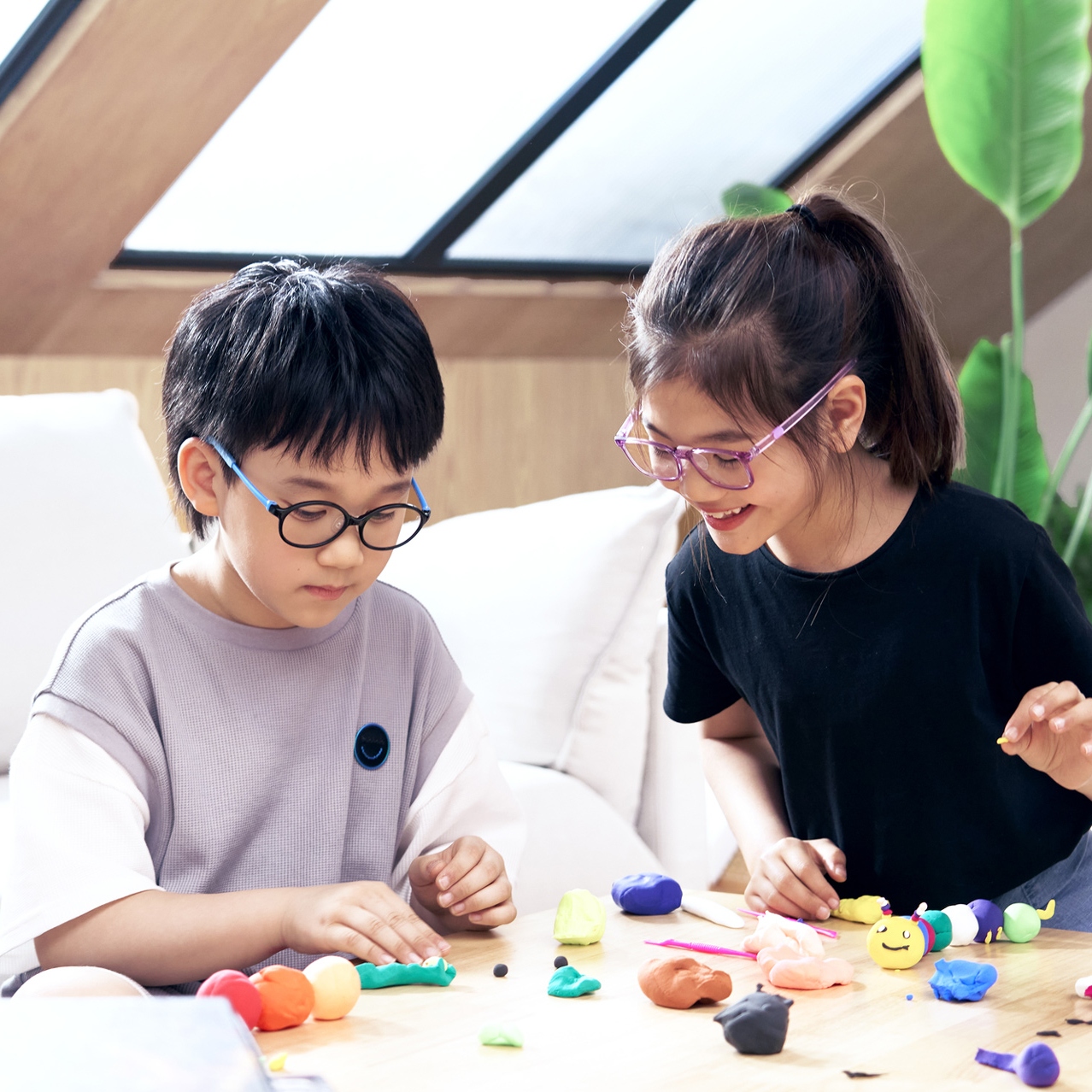 Two children wearing ZEISS Myopia Management lenses playing with modeling clay on a table.