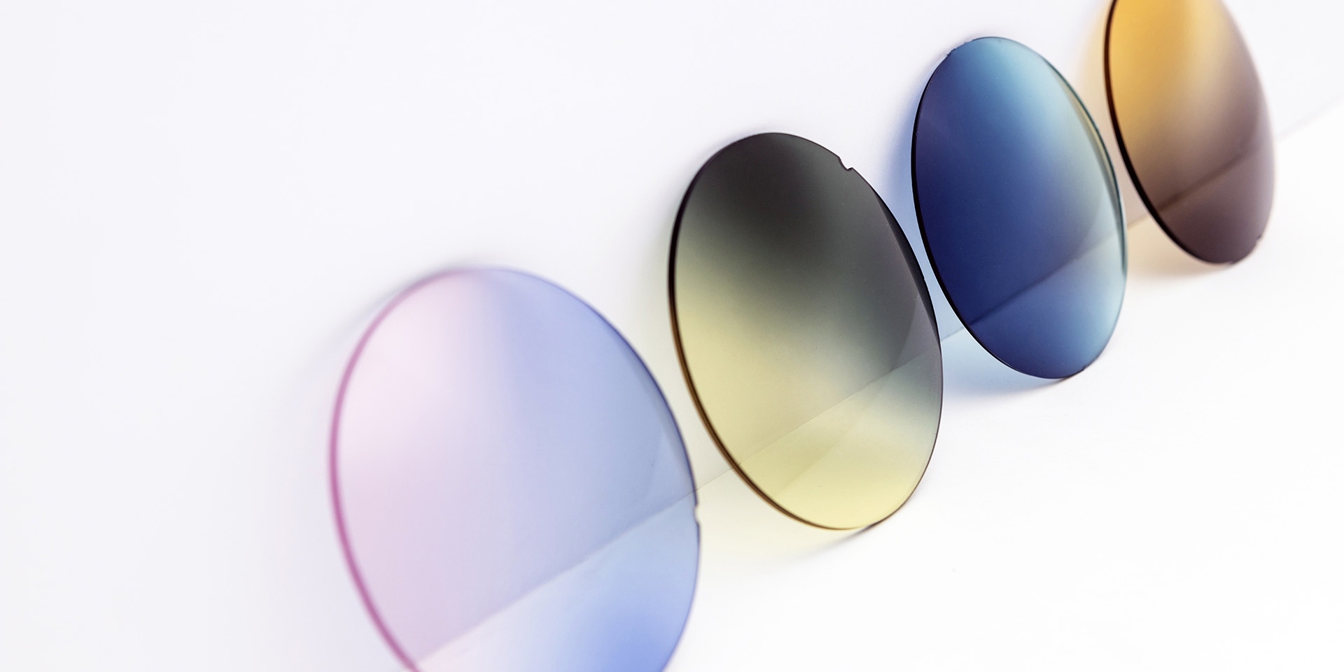 Different coloured sunglass lenses leaning against a white surface: pink-purple, yellow-grey, blue and brown gradients.